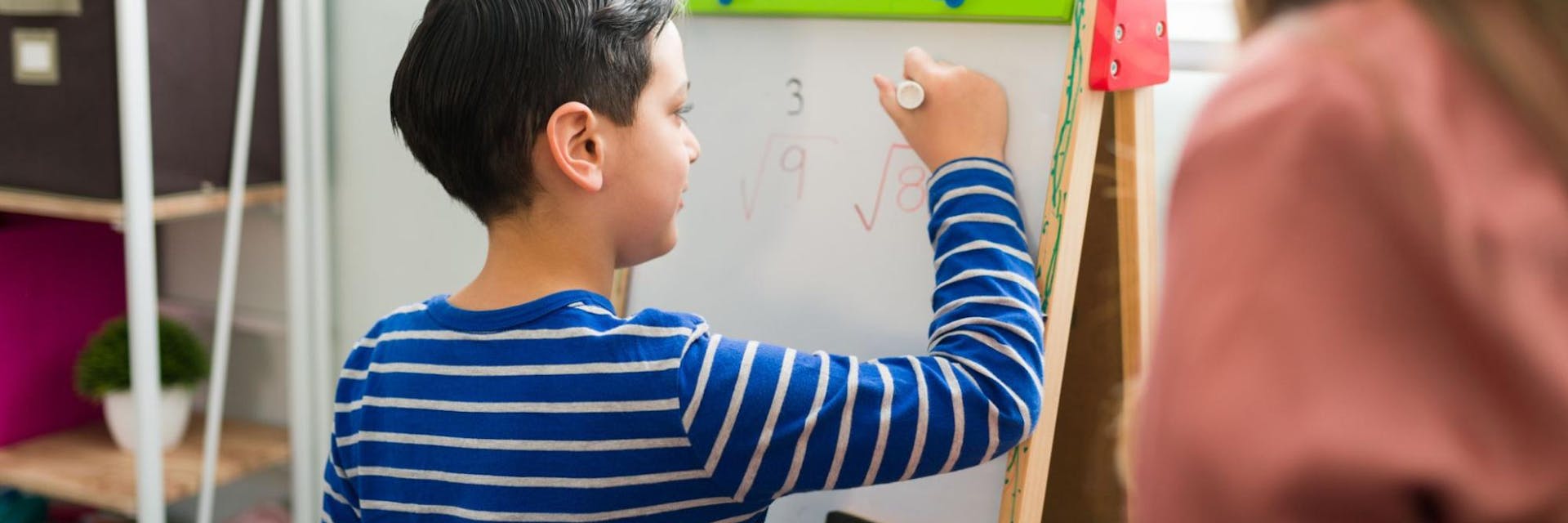 Young boy practices long division games on a whiteboard in his classroom. 
