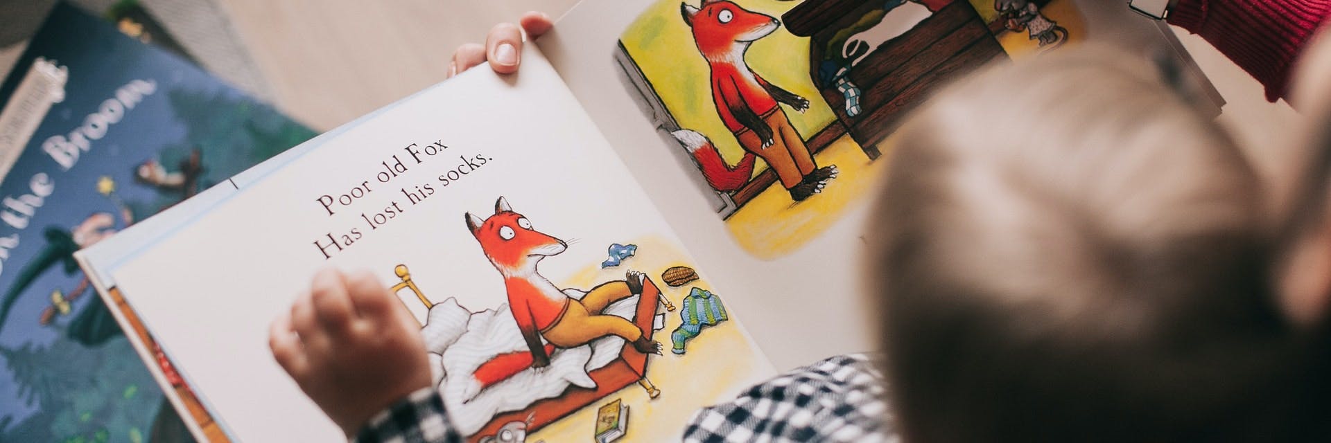 A young child reads a book about a fox in an overhead picture. 