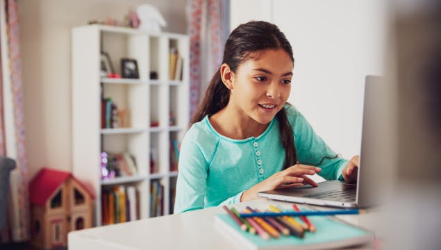 An elementary student working on a laptop in her bedroom.