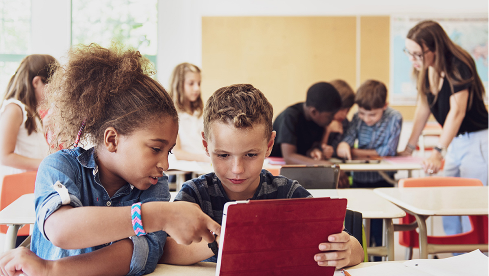 Two elementary students looking at a tablet in class.
