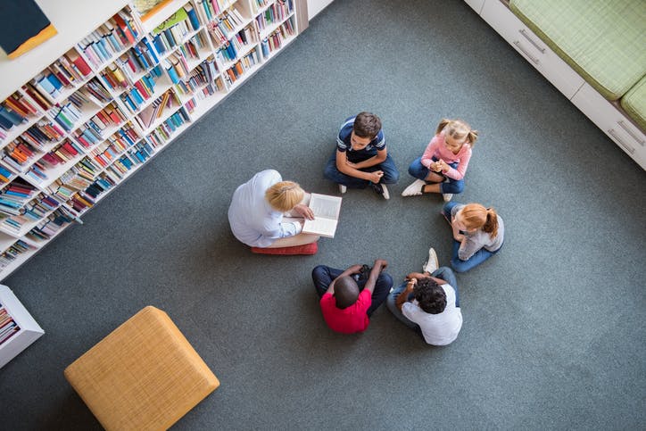 Elementary school teacher reading to a group of five students.