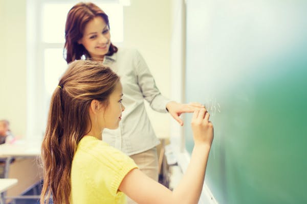 A female teacher is instructing student math on a blackboard