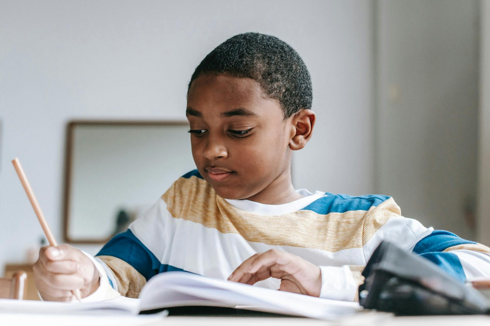 A young boy sits in class and completes vocabulary activities in a workbook with a pencil. 