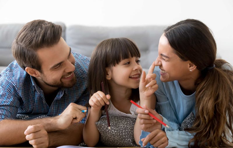 Child smiles and plays with her parents as they write in a journal together.