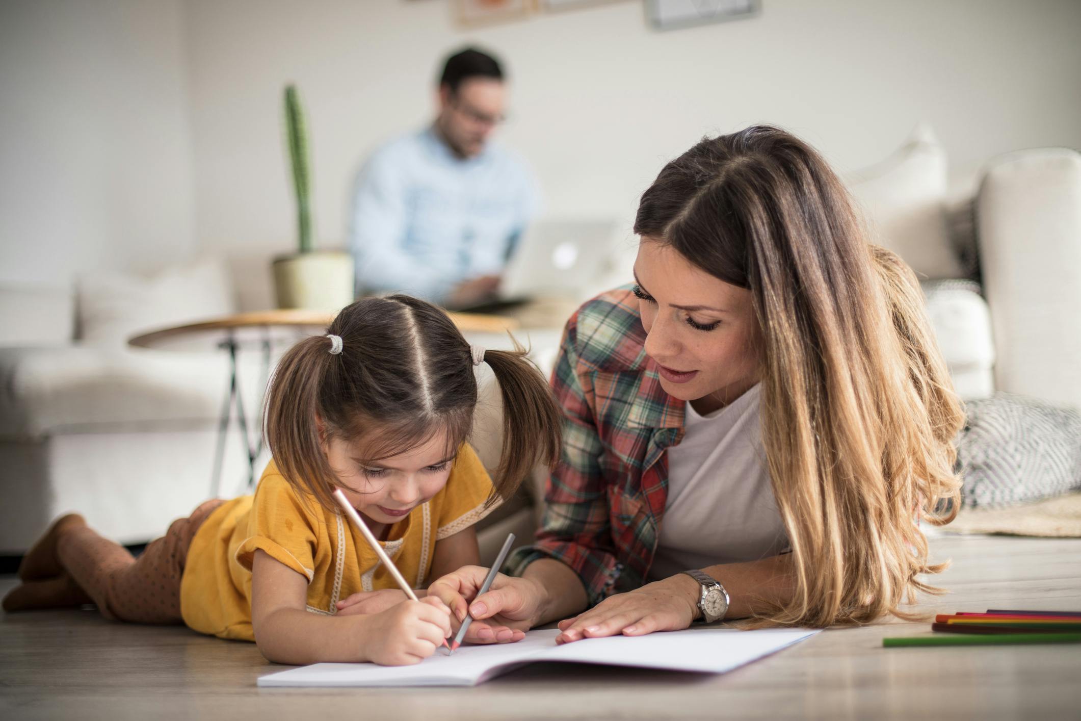 Mom helping her young daughter write notes in a notebook.