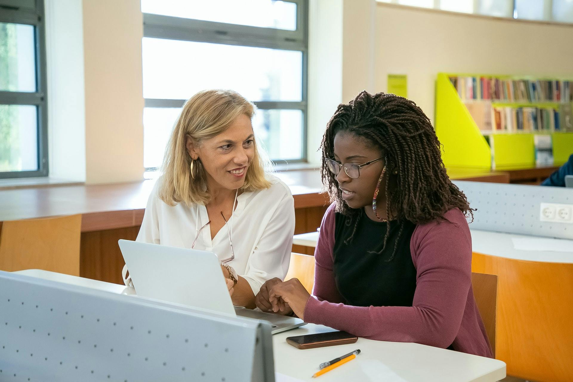 Two teachers sit in a classroom and look at a classroom website on a laptop computer. 