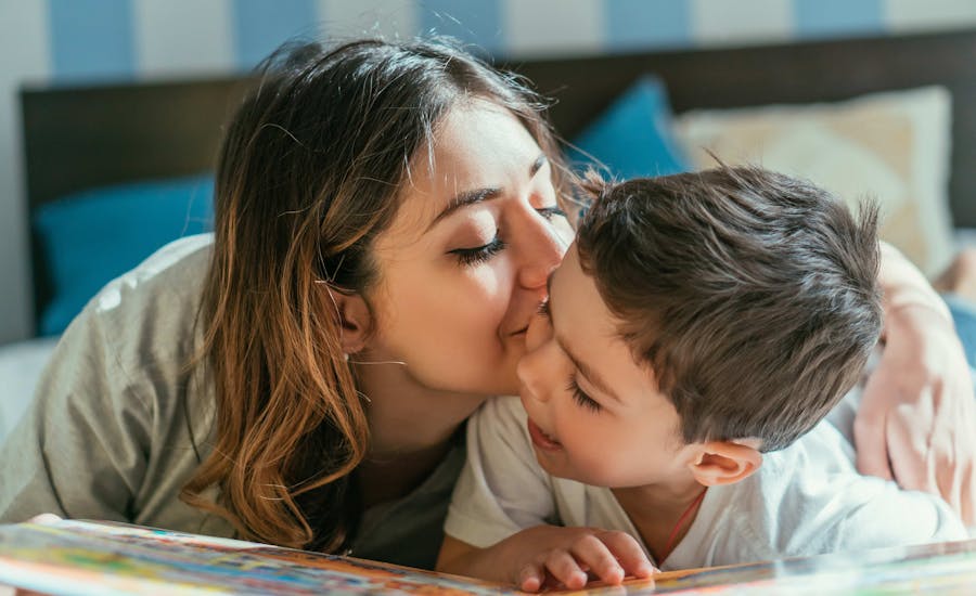 Mom kisses her child as they sit together.