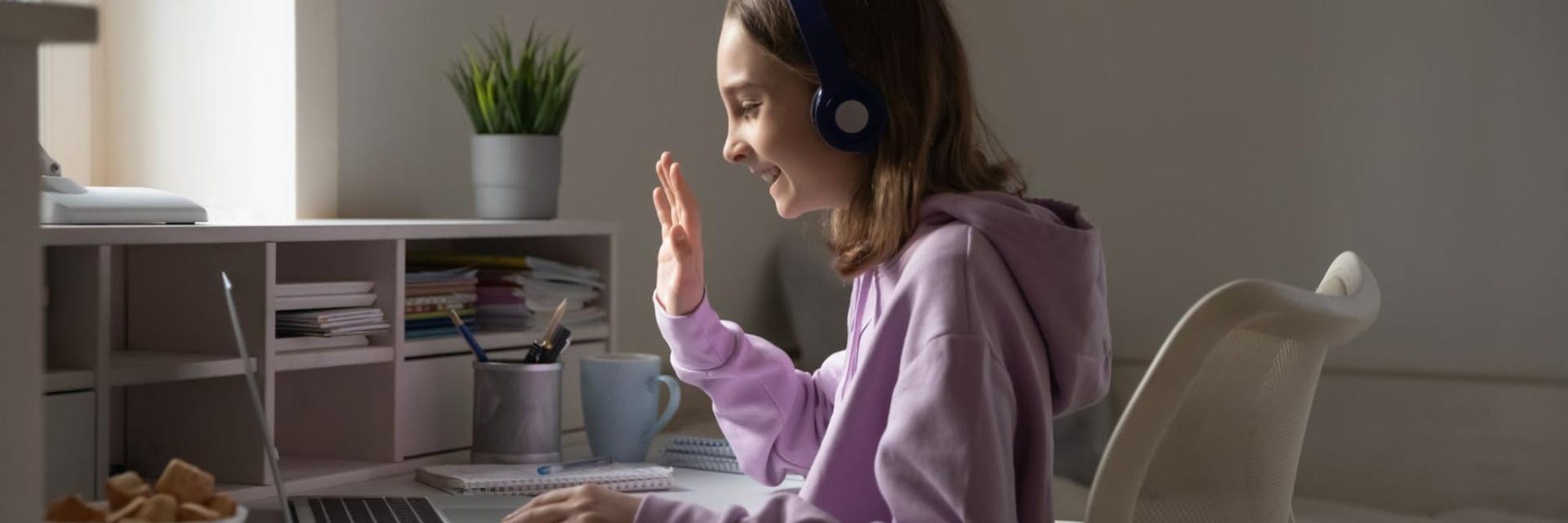A young girl waves at her math tutor while sitting in her room on her computer.