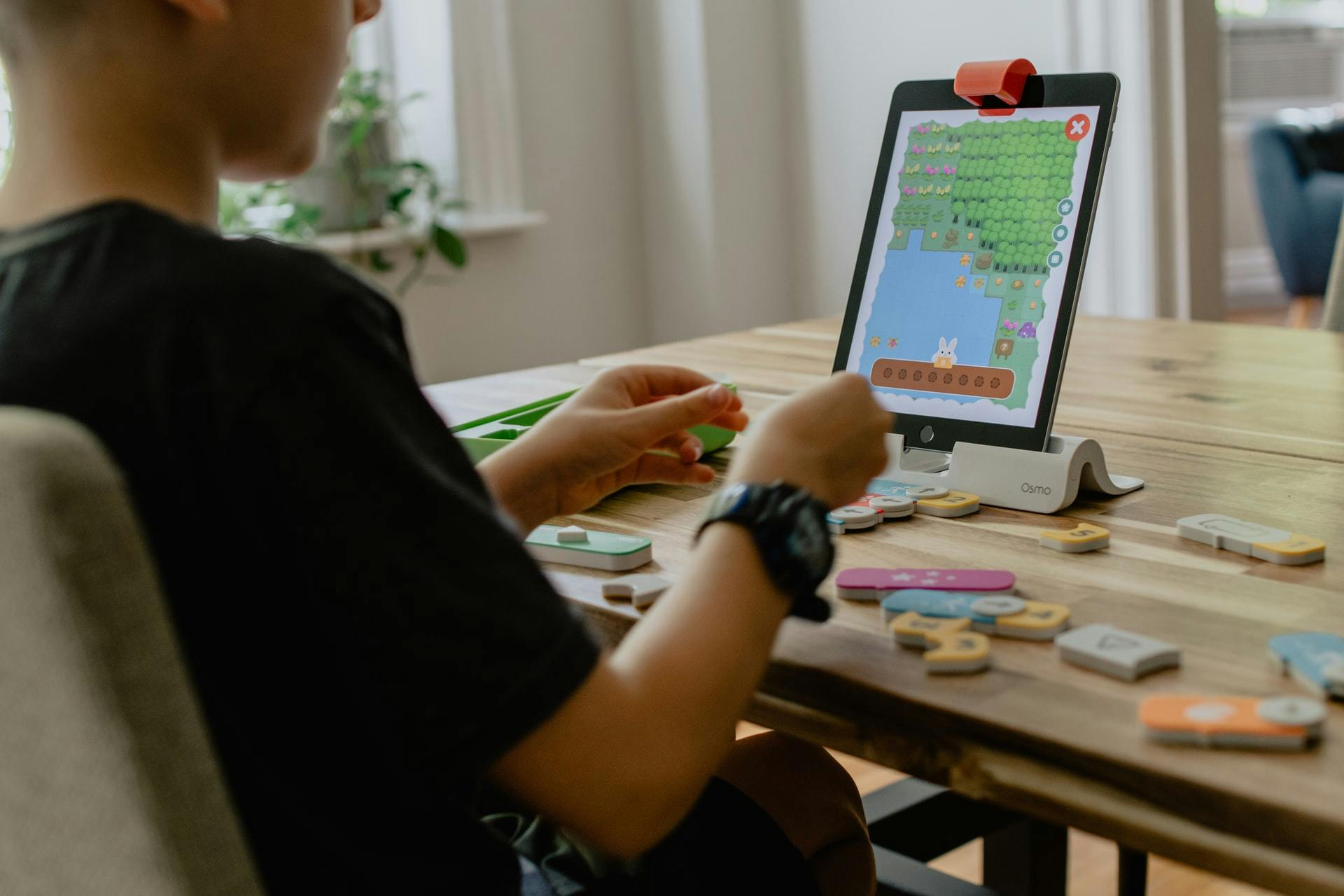 Young boy plays with an online learning game on a tablet while sitting at a kitchen table.