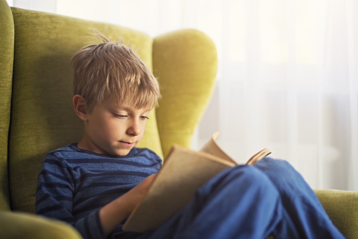 Child reading a book from his reading log in an armchair.