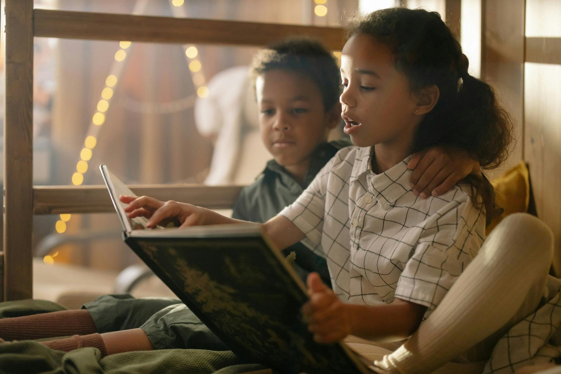 Two kids reading a book together at an age-appropriate reading level.