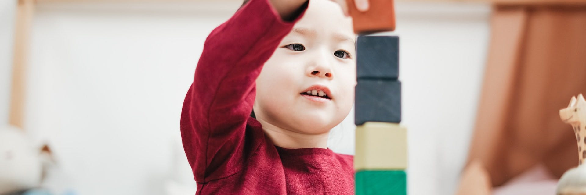 A young child plays with wooden blocks in a play-based learning classroom.