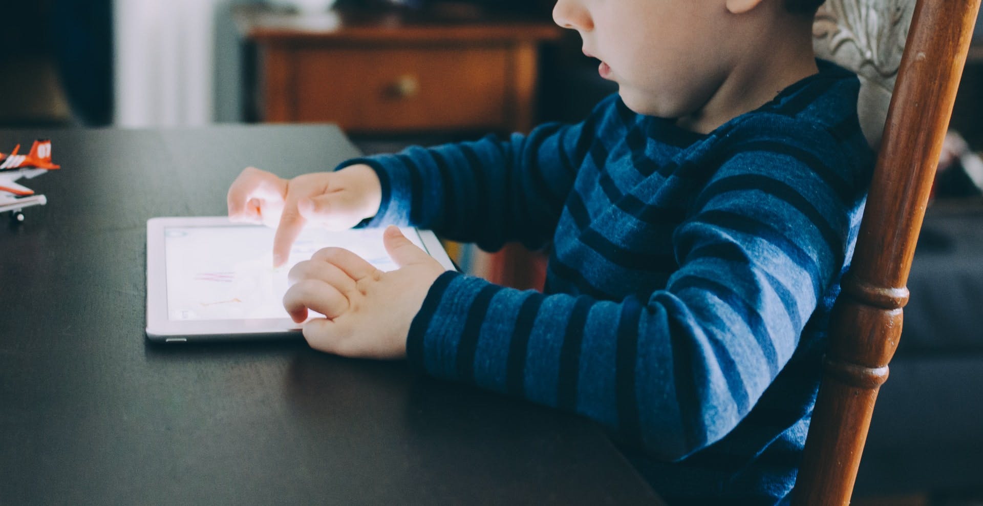 Young child plays online word games on a tablet while sitting at a table.