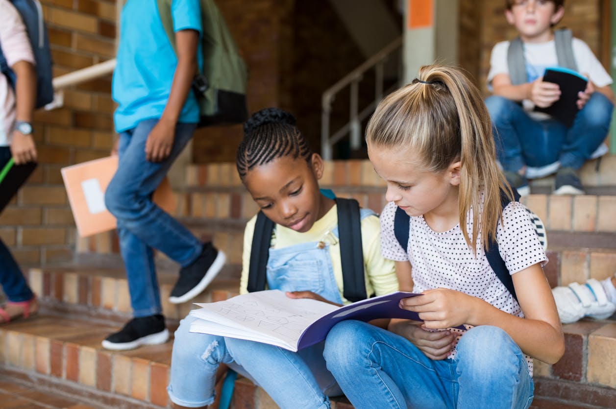 Two students working on homework together, on the steps outside of their school building.