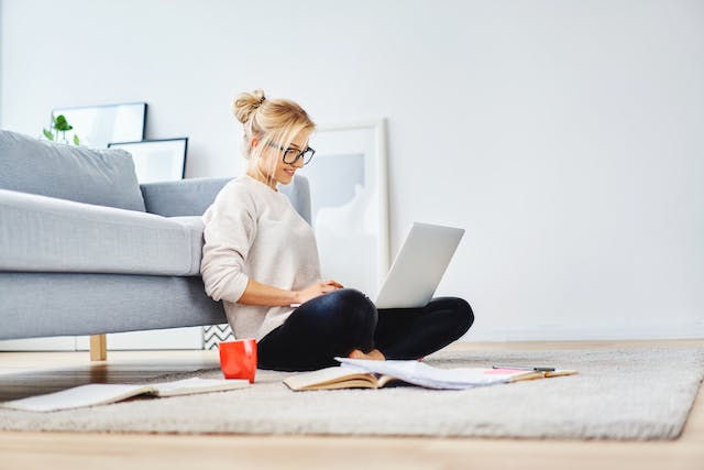 Woman sitting in front of her couch on laptop.