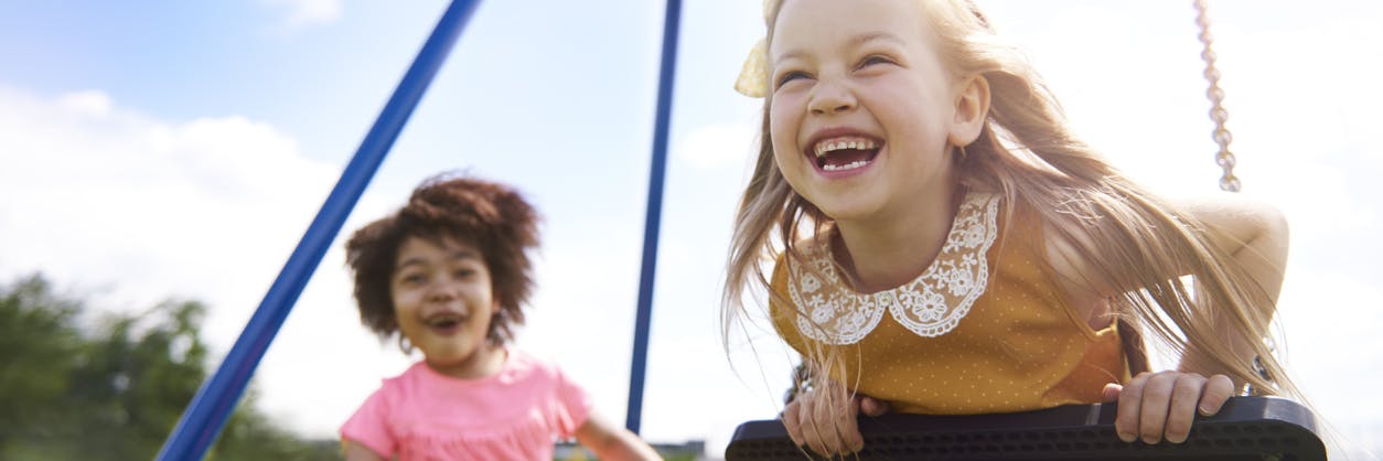 Two girls play outside on a playground during a playdate.