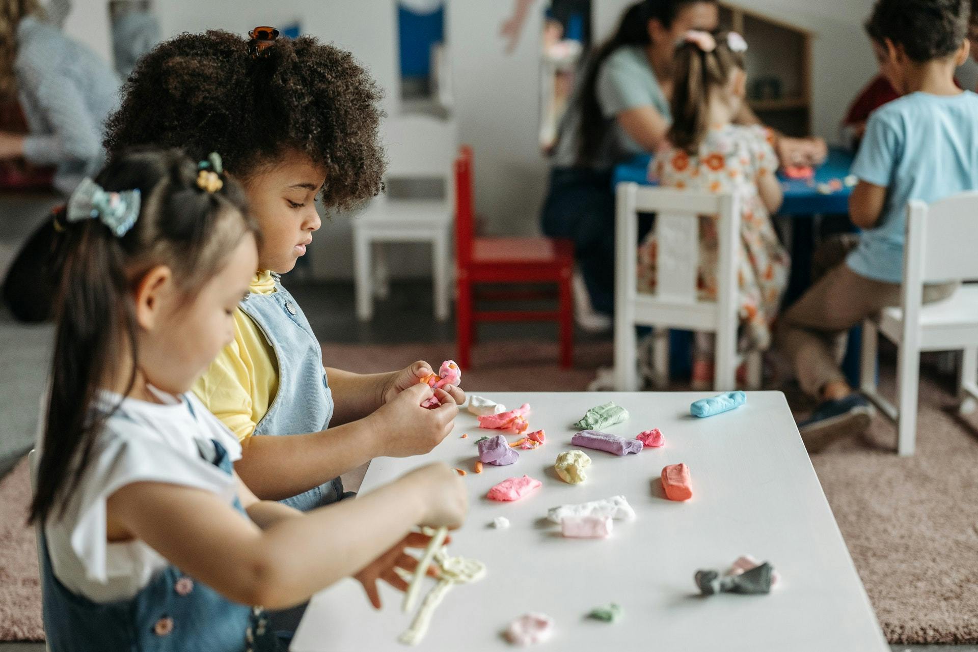 Two young girls play with playdough in a play-based learning classroom. 