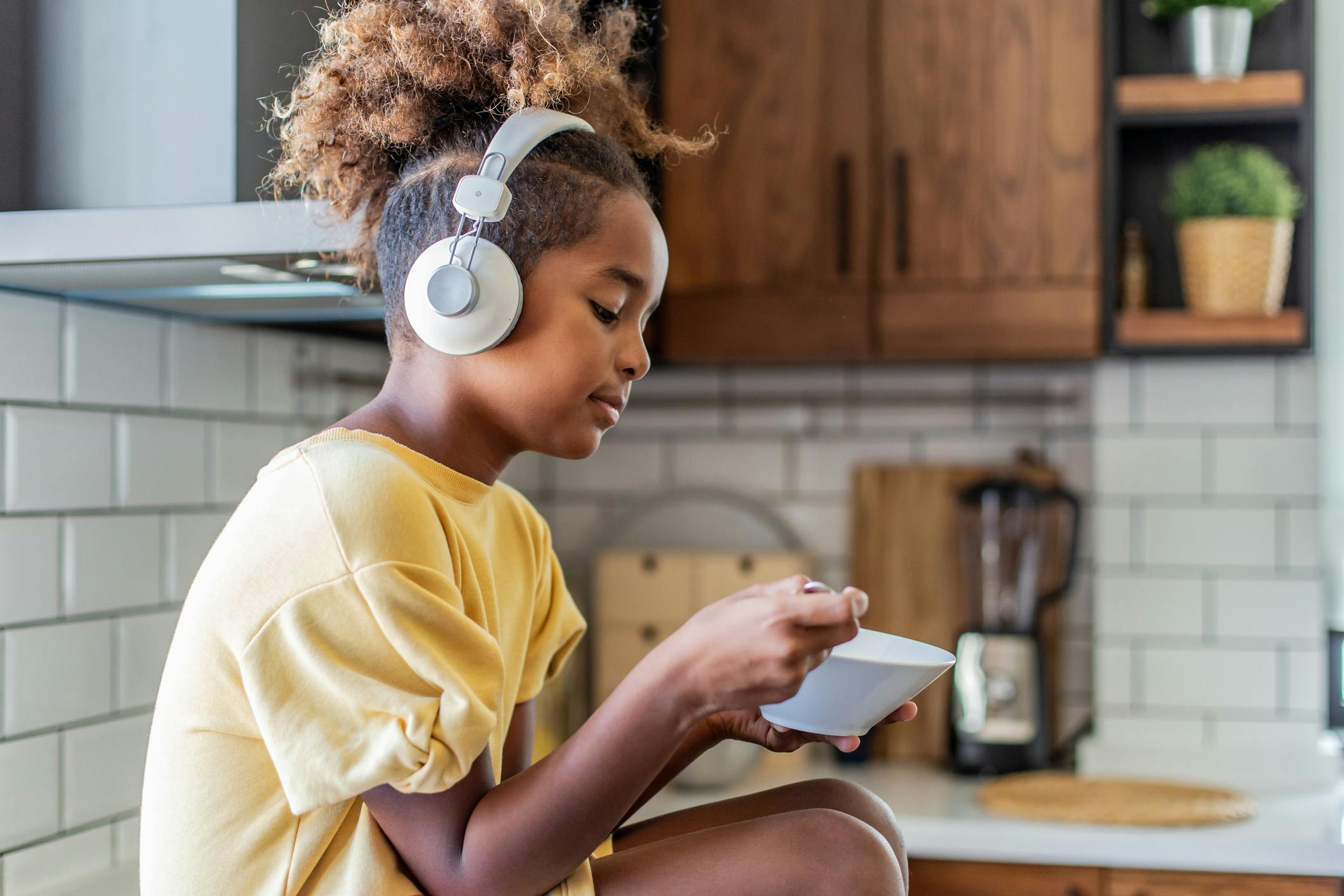 Young girl wearing headphones in her kitchen.