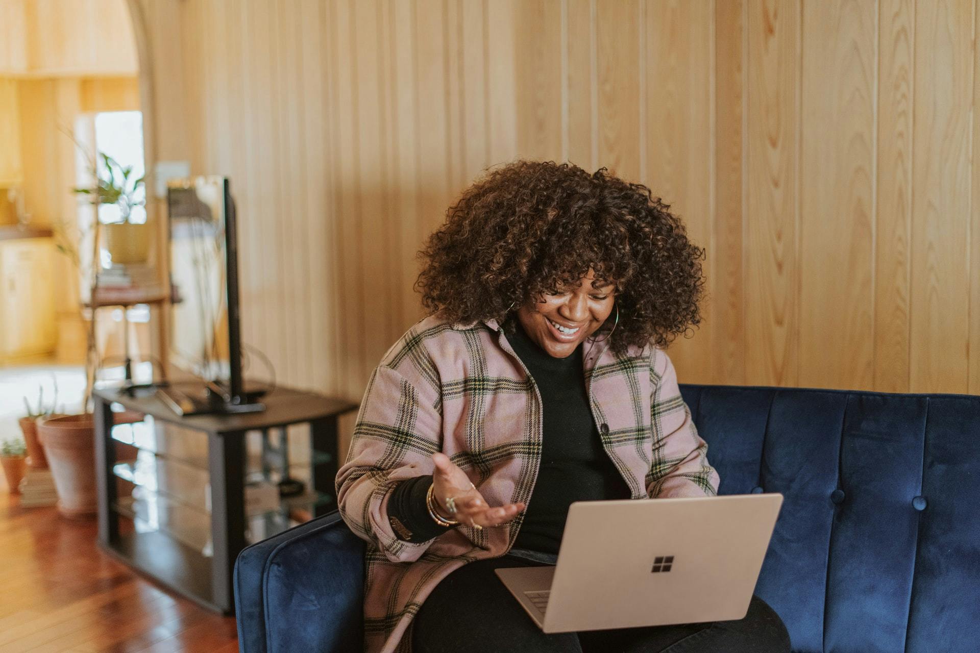 Woman sits on couch in her home and works on a laptop computer while she learns virtually.