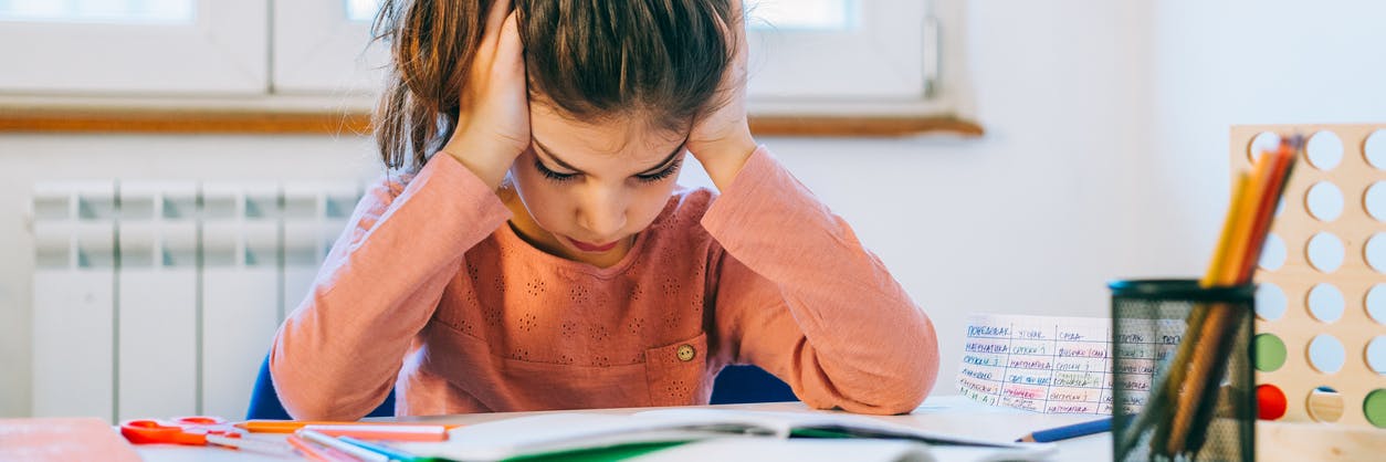 Frustrated child sitting at a desk, struggling with her school work.