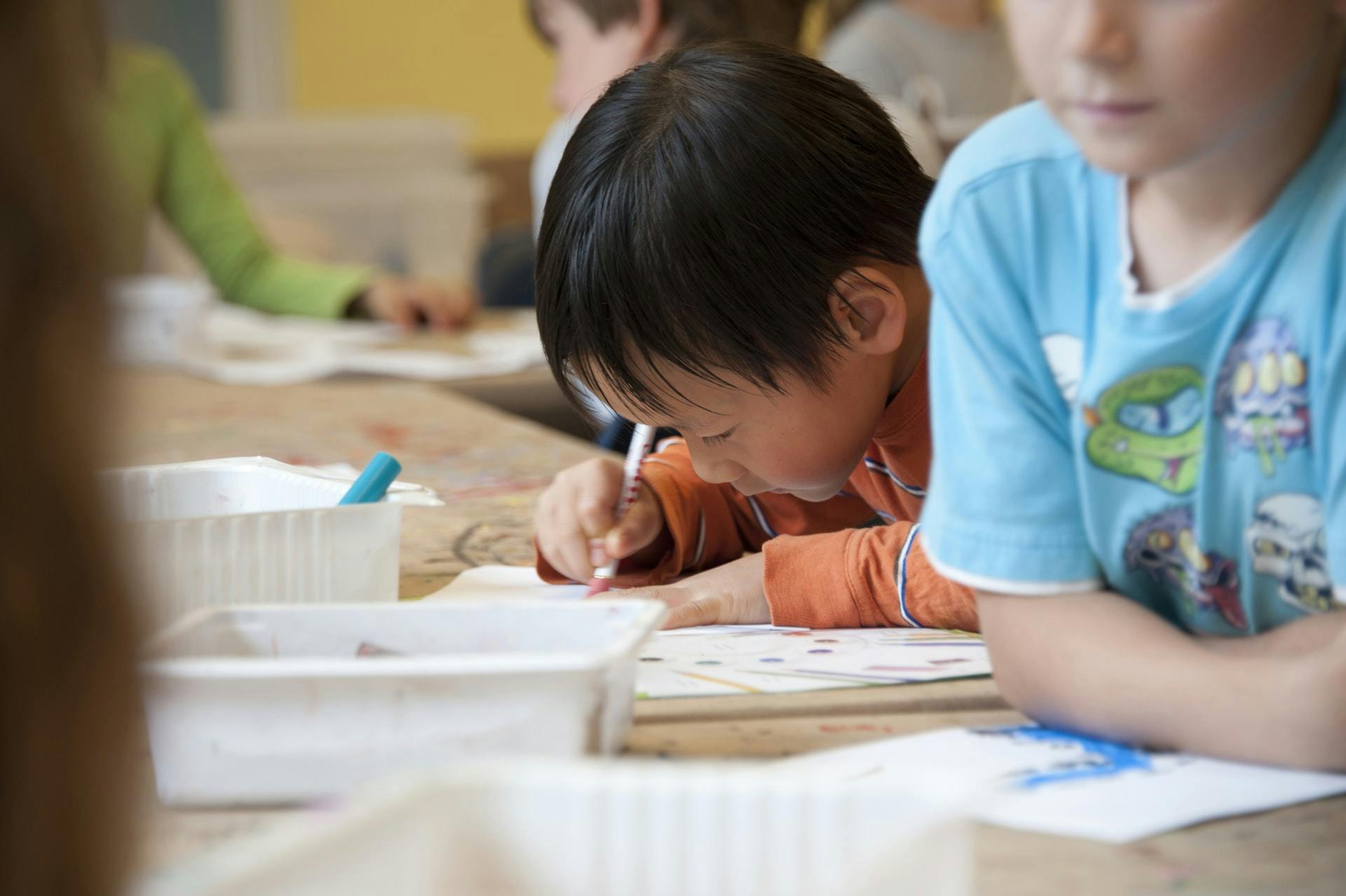 A young student, working at a table filled with other students, works on a vocabulary activities worksheet.