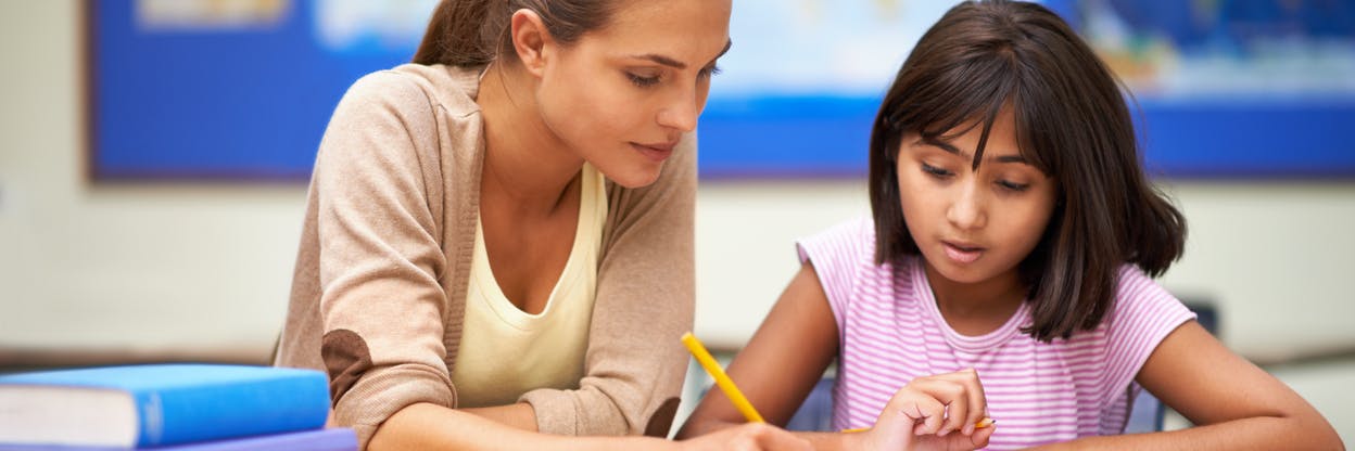 Child and her math tutor working together to solve a math problem in her notebook.