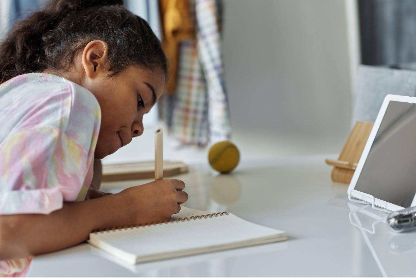 Child studying at a desk with a tablet device in front of her.