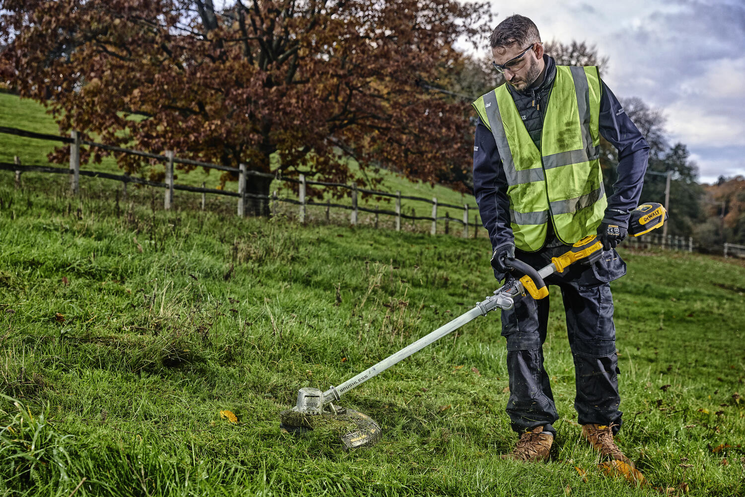 Person i verneklær trimmer gress med Dewalt DCMST561N-XJ
