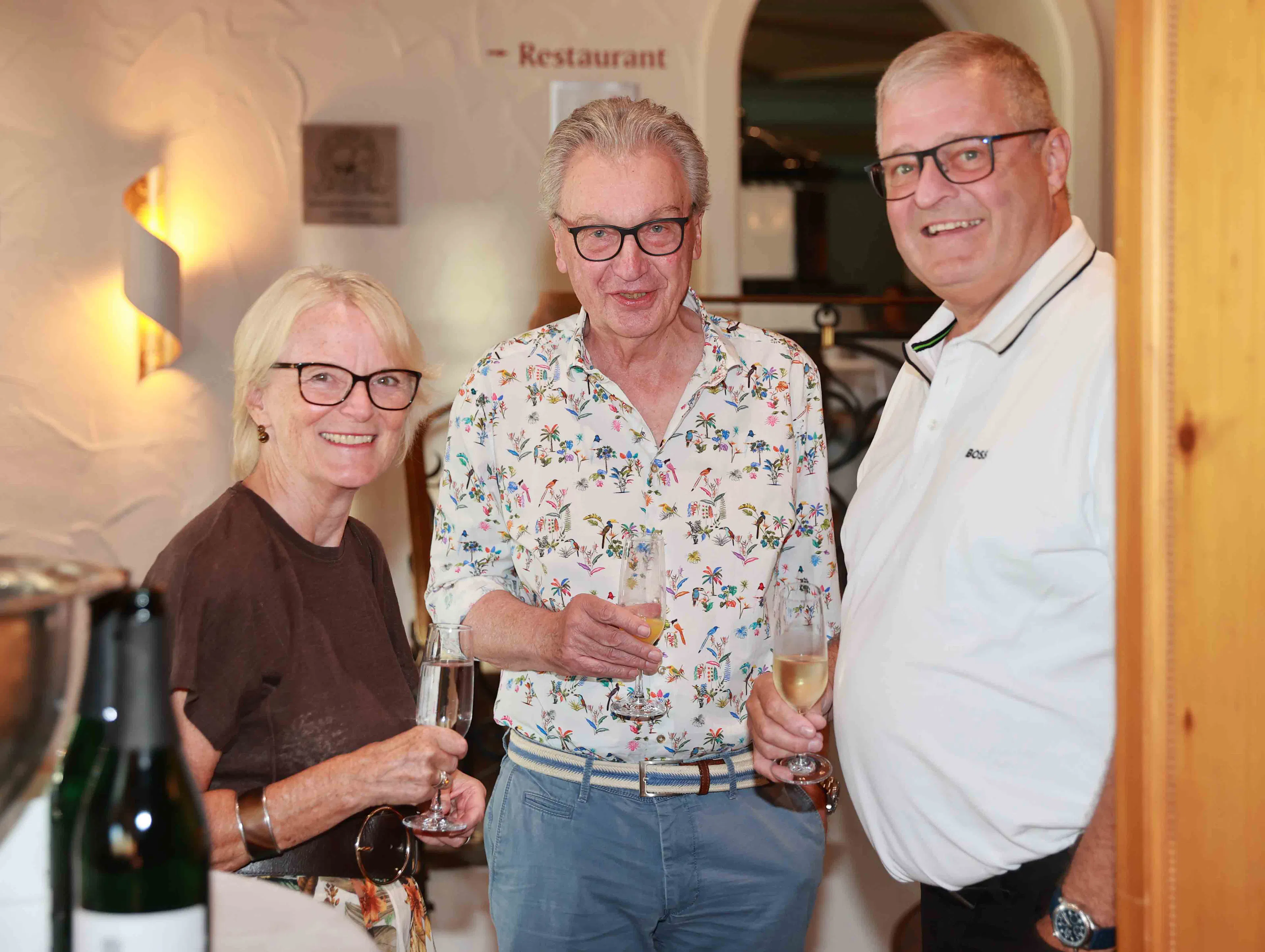 Drei Senior:innen stoßen in gehobenem Restaurant mit Sekt ans