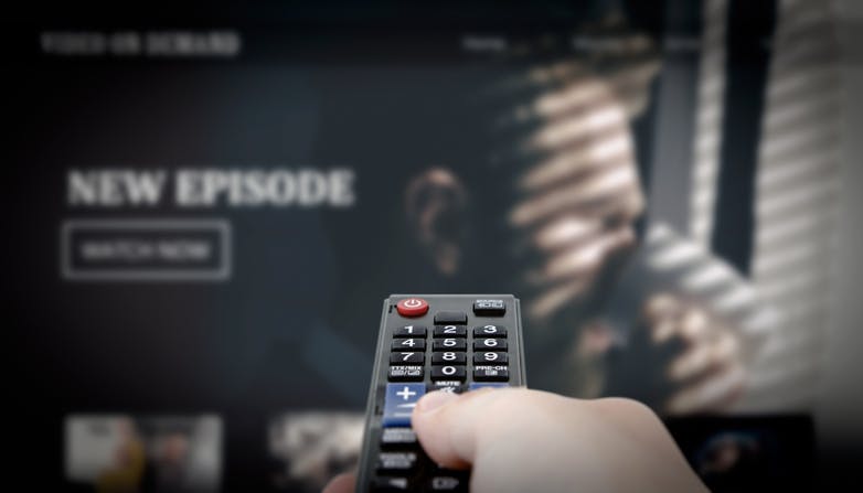 Pessoa com controle remoto na mão para assistir novo episódio de uma série na TV