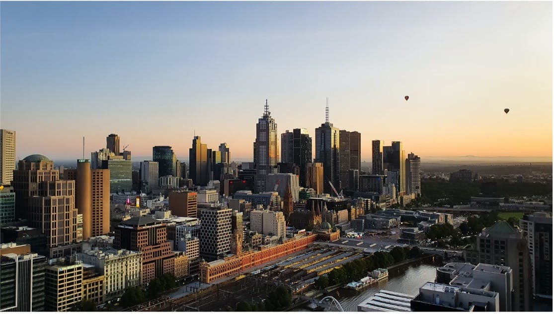 Skyline view of Melbourne as the sun rises with hot air balloons in the distance
