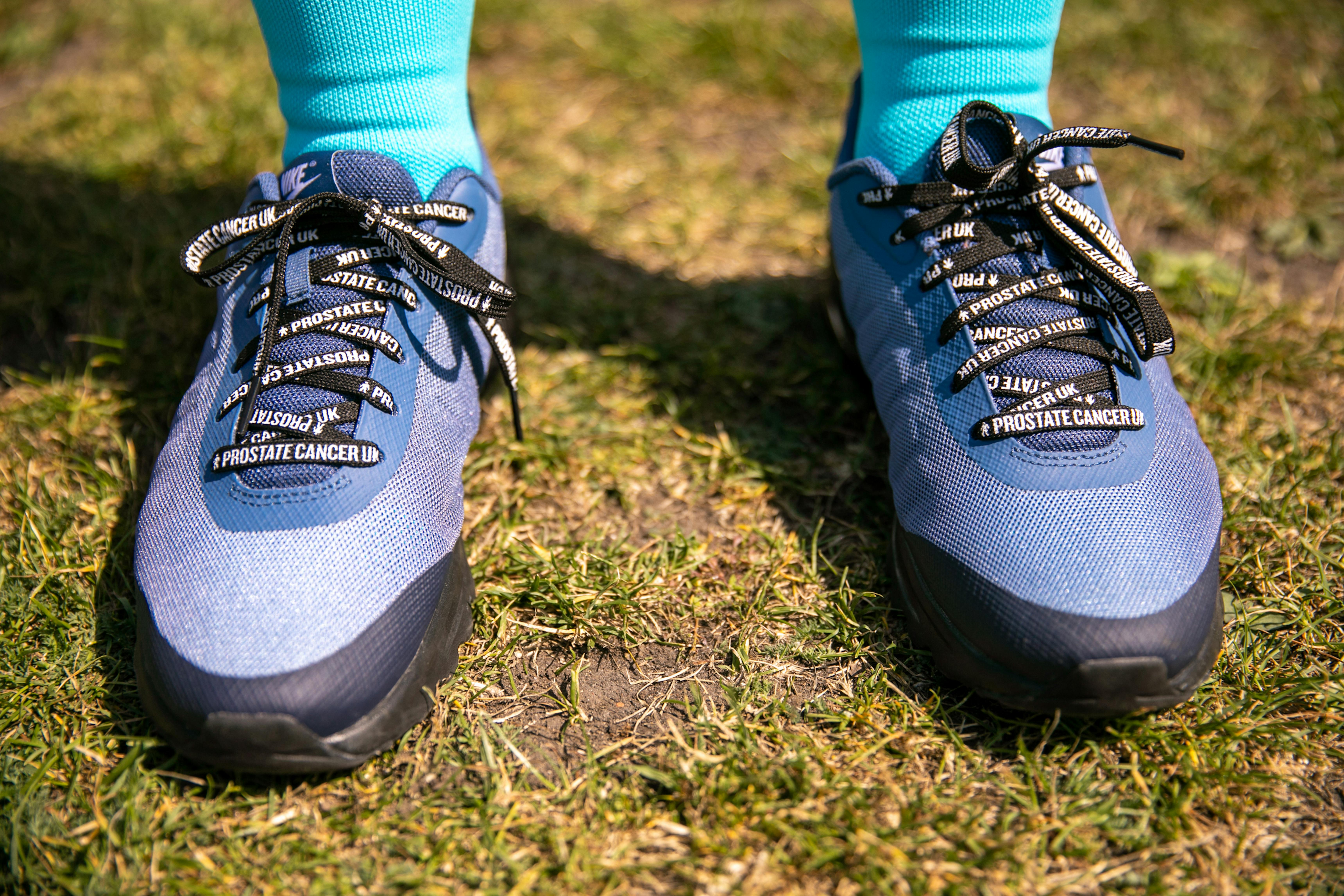 A pair of blue trainers laced with Prostate Cancer UK branded shoelaces. 