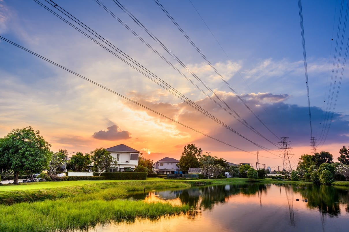 Linie energetyczne nad domami, na tle zachodzącego słońca