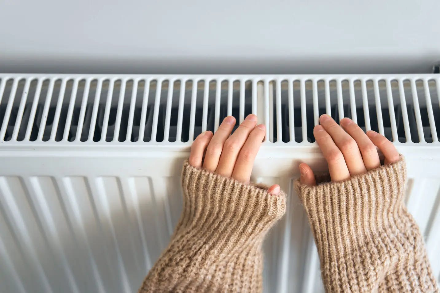 Dłonie w beżowym swetrze ułożone na białym grzejniku