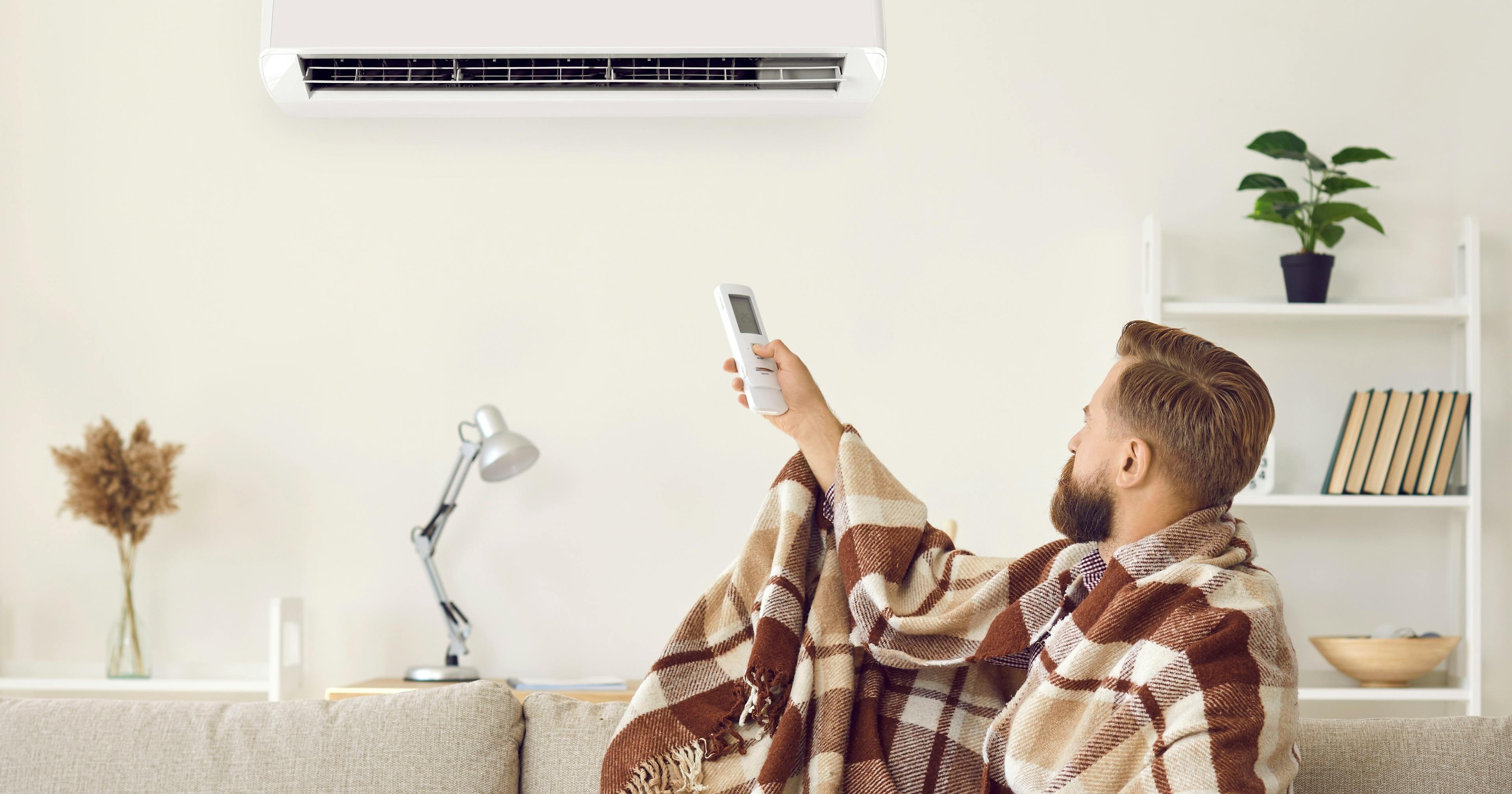 Mężczyzna w domowym wnętrzu włącza tryb grzania klimatyzatora