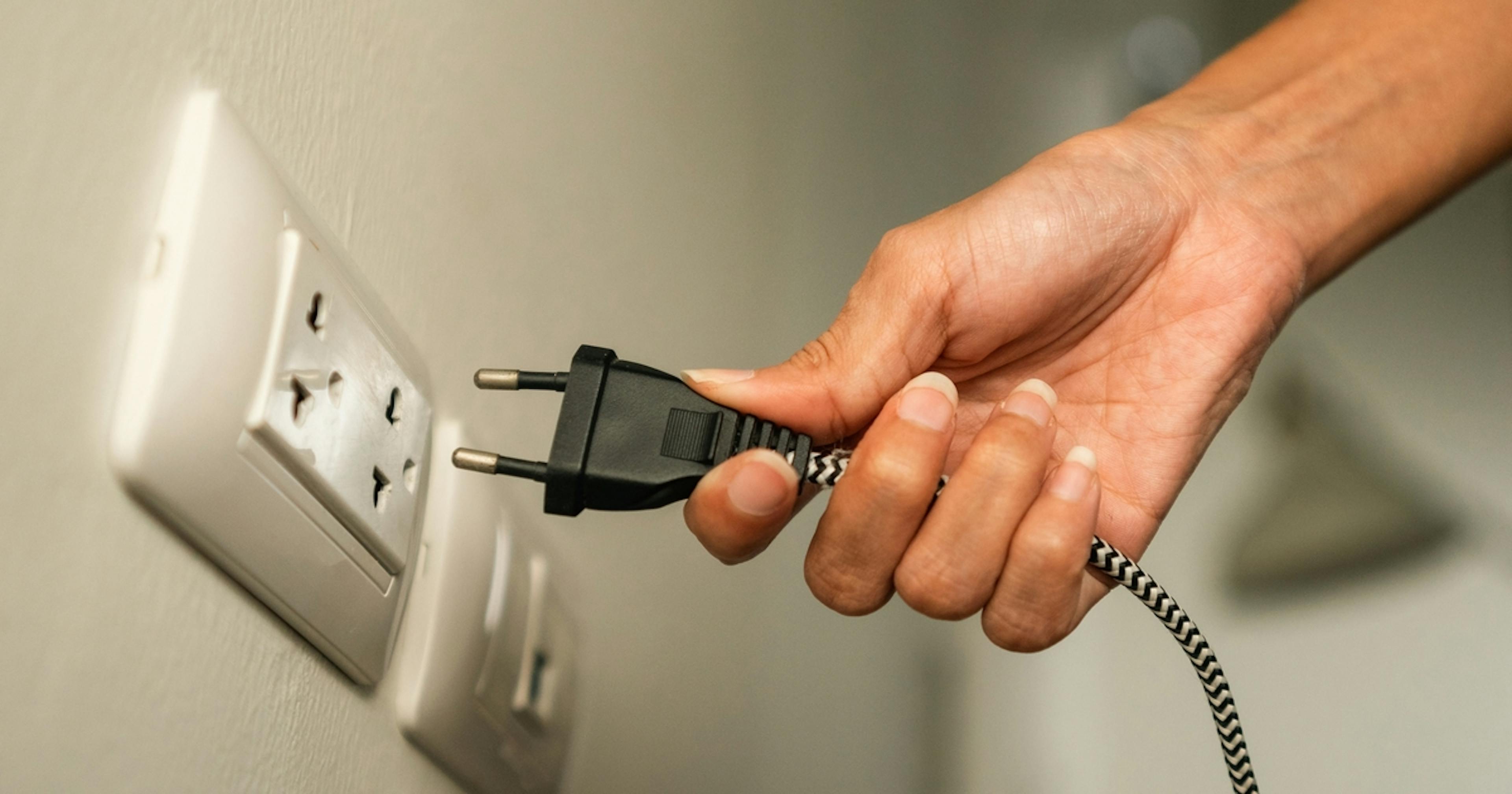 Zdjęcie ręki wyjmującej wtyczkę urządzenia elektrycznego z kontaktu