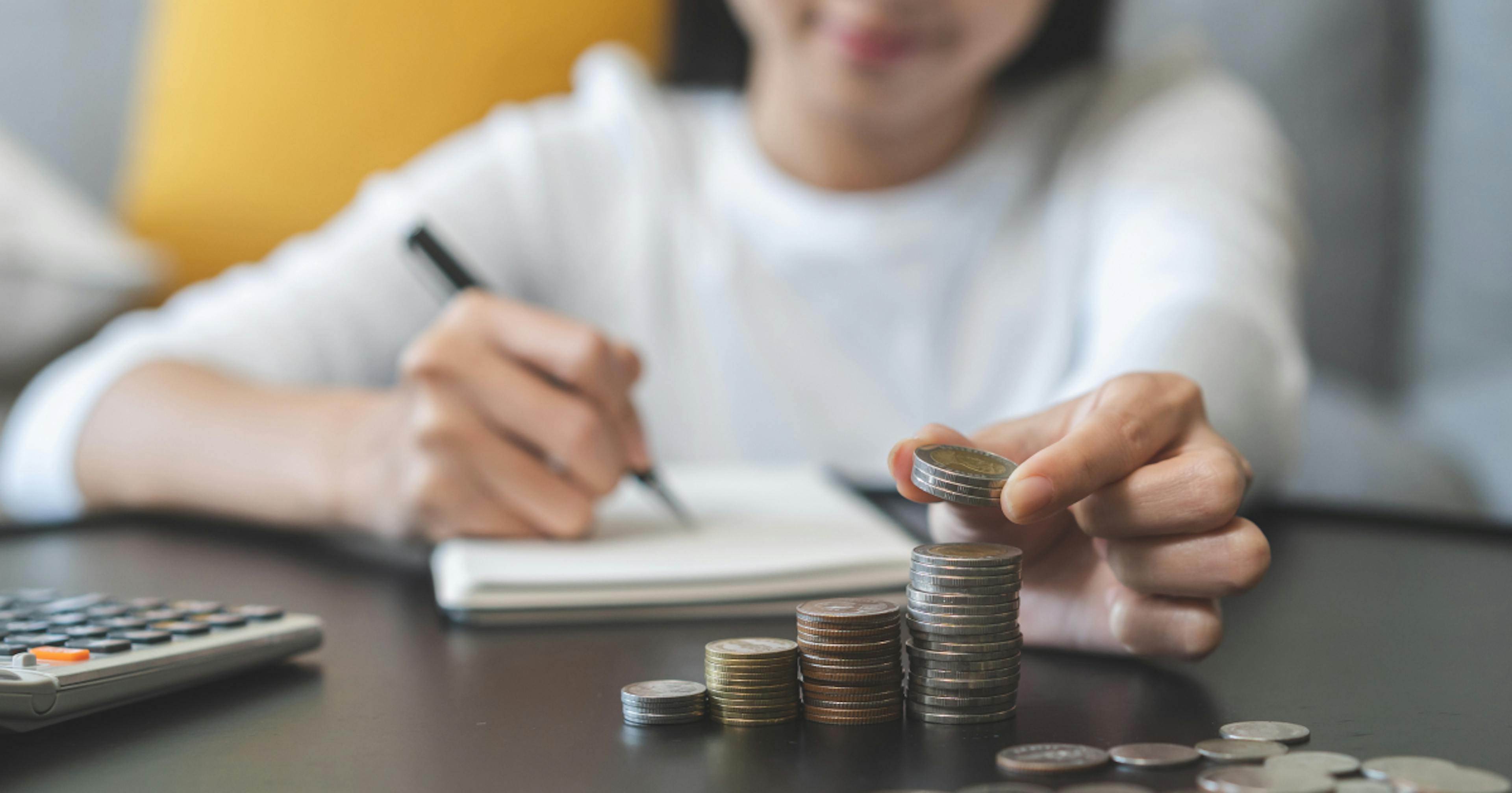 Osoba licząca monety i zapisująca wydatki w notesie 