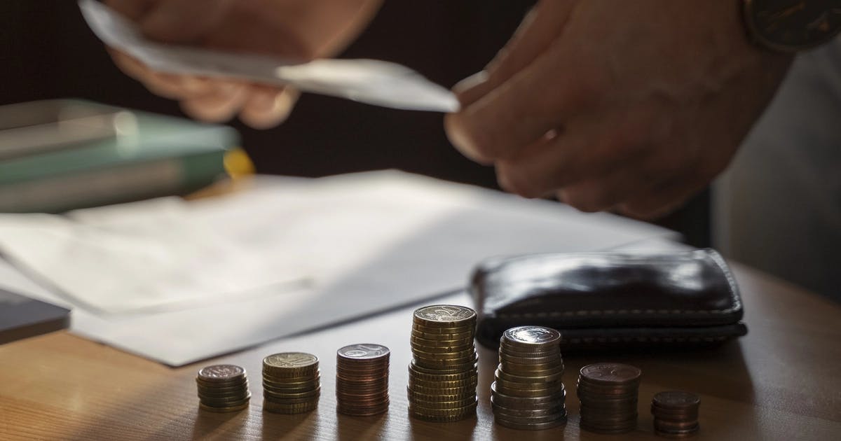 Stosy monet na stole i dłonie osoby przeglądającej rachunek