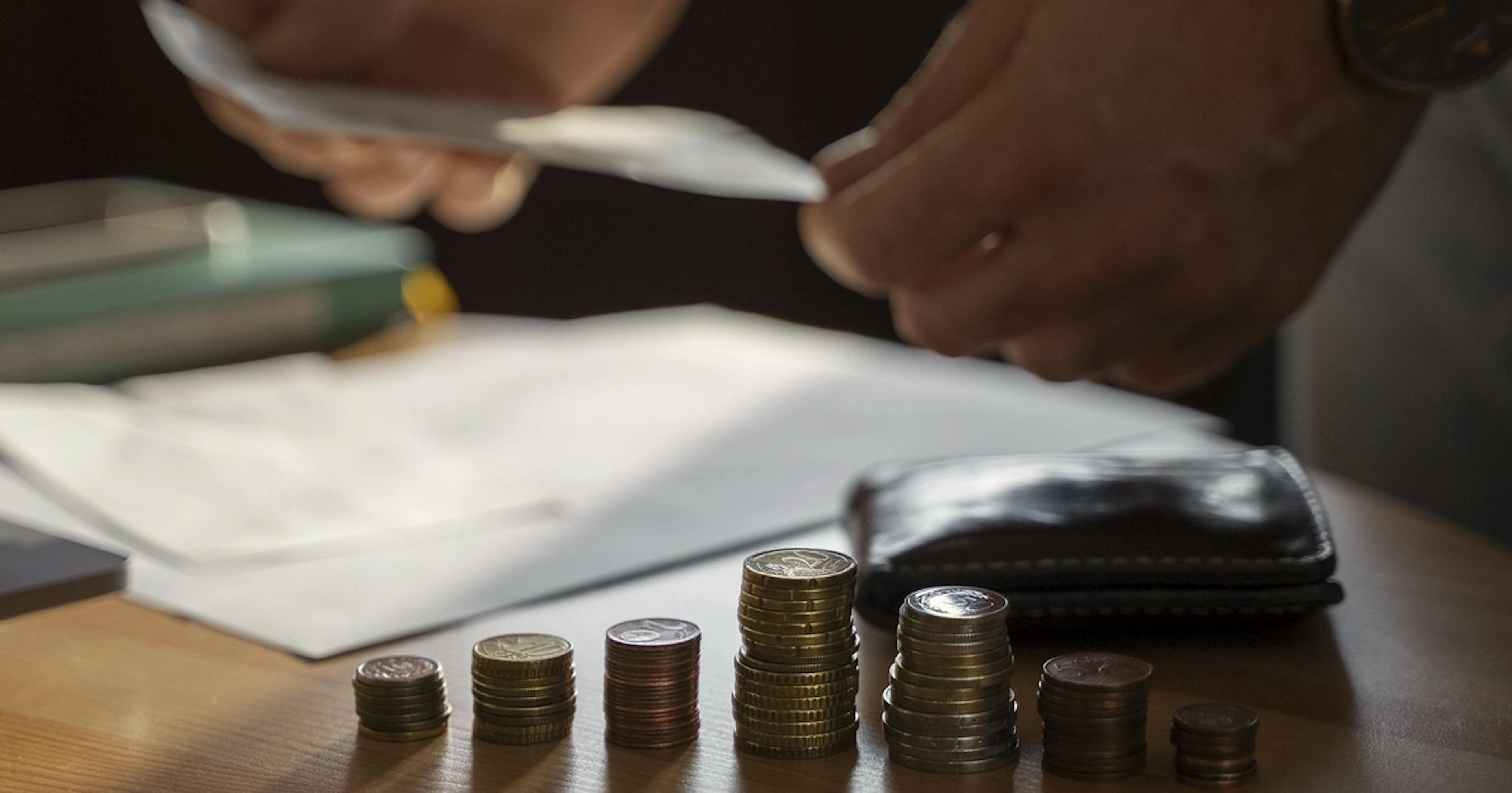 Stosy monet na stole i dłonie osoby przeglądającej rachunek