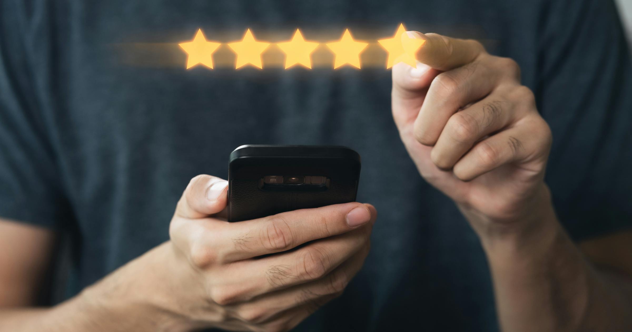 Osoba trzymająca smartfon wskazuje na rząd pięciu gwiazdek symbolizujących wysoką ocenę lub opinię.