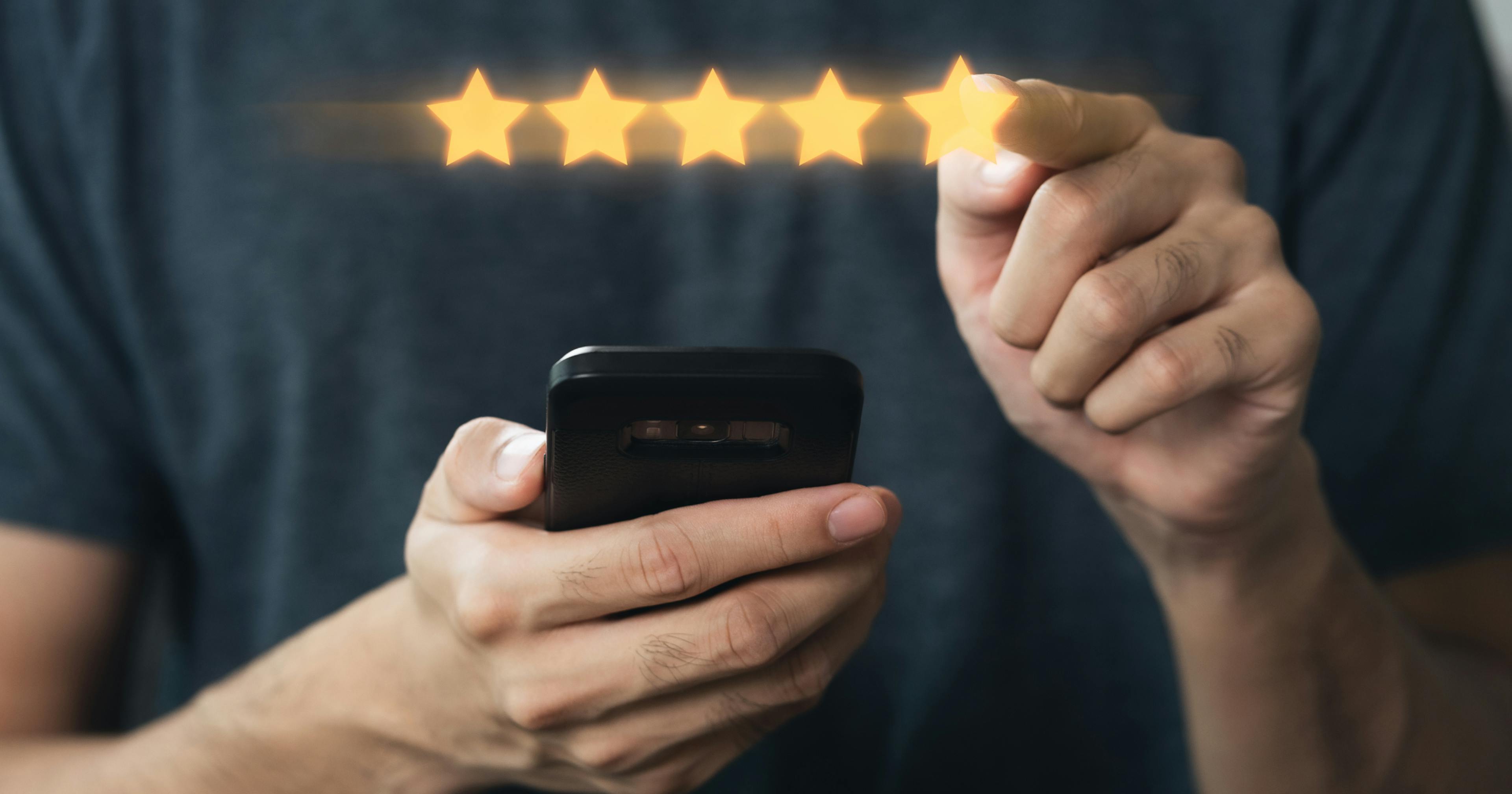 Osoba trzymająca smartfon wskazuje na rząd pięciu gwiazdek symbolizujących wysoką ocenę lub opinię.