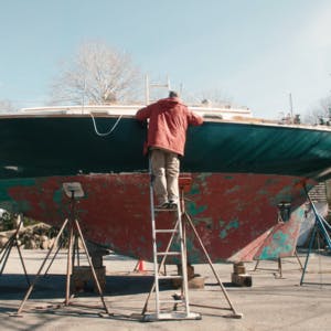 A person on a ladder working on a boat in a drydock