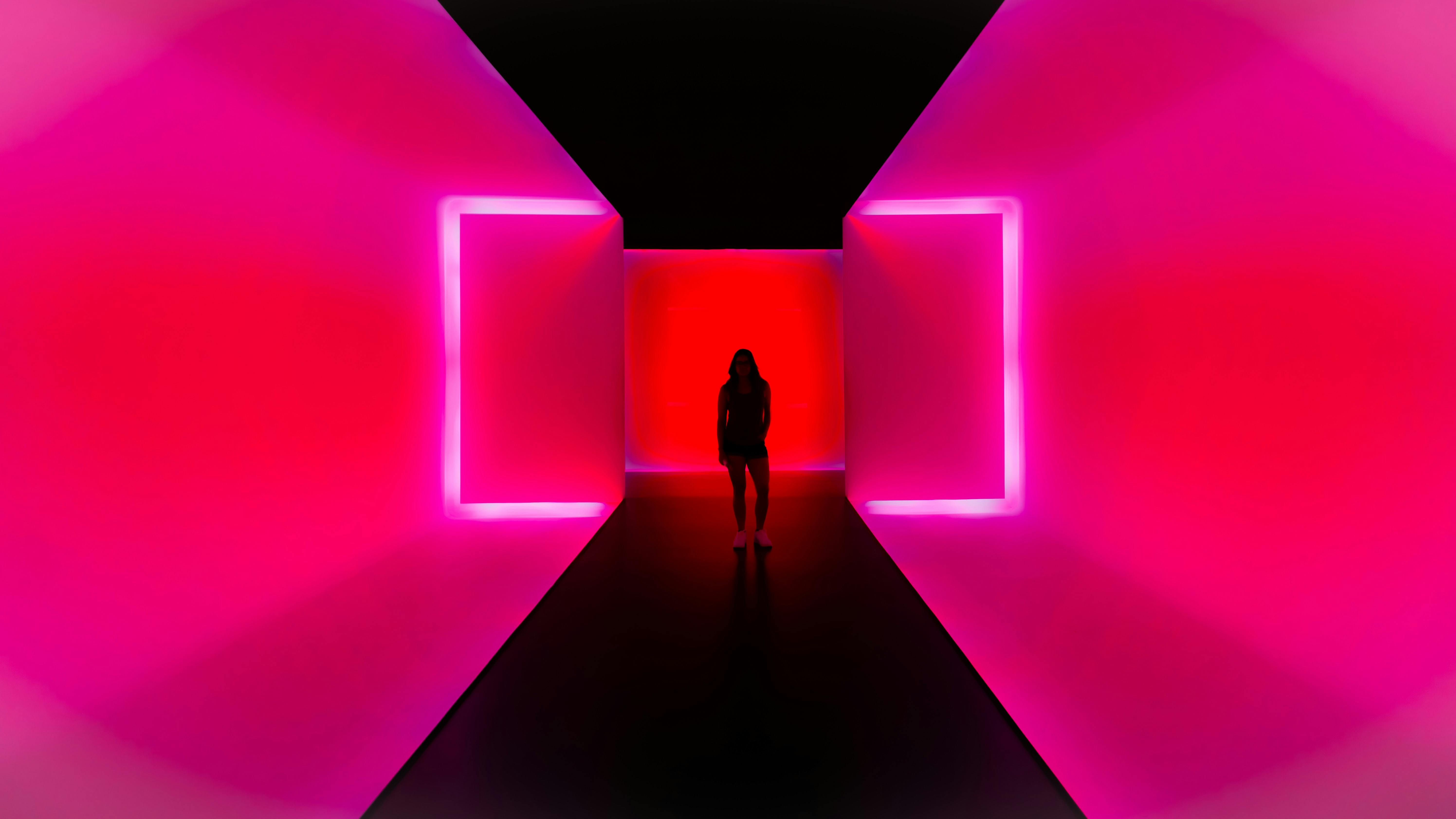 A person standing in a middle of a dark hallway with pink lit walls