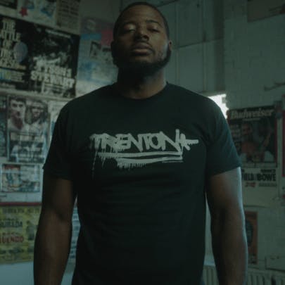 A man with a shirt that shows the Trenton logo standing in a room