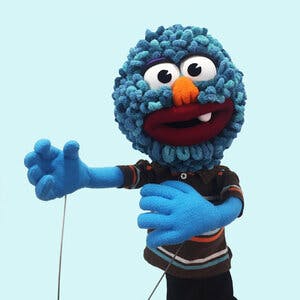A blue puppet standing in front of a light blue background