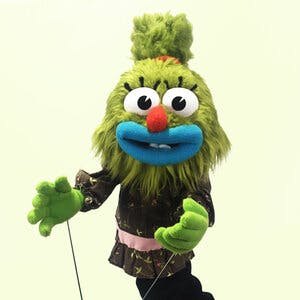 A green puppet with blue lips standing in front of a light green background
