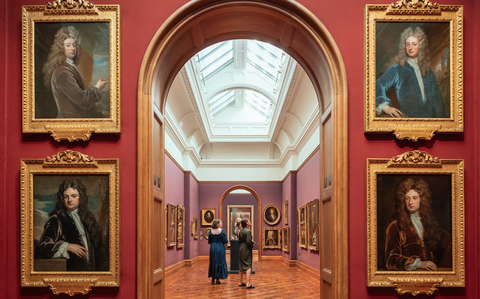 Art gallery, red walls, parquet floor, 18th century portraits of men with big hair
