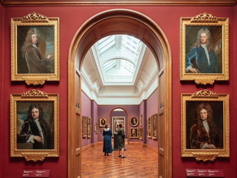 Art gallery, red walls, parquet floor, 18th century portraits of men with big hair