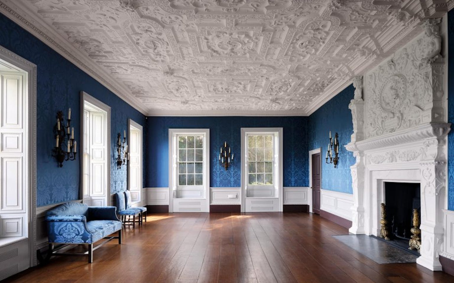 A highly decorated plaster ceiling with blue damask walls and wooden floor