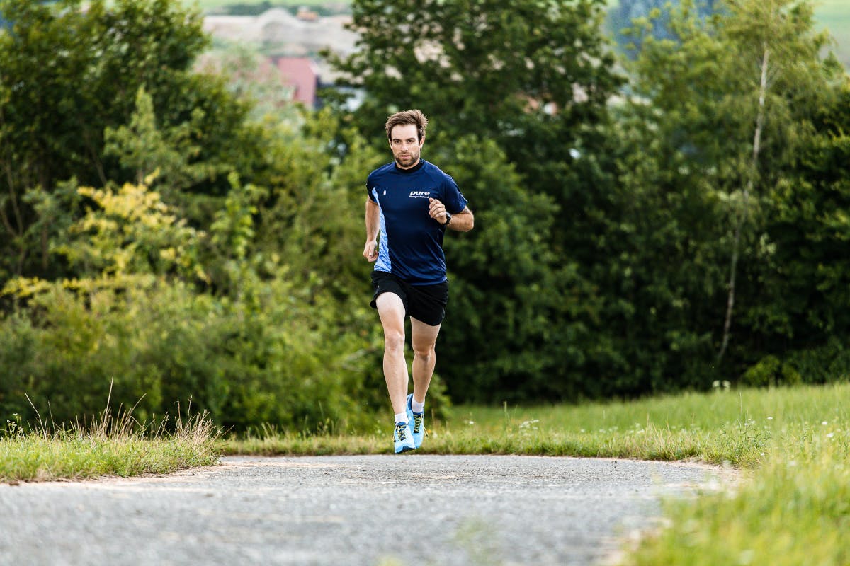 Ein Läufer im blauen Sportoutfit läuft in der grünen Natur